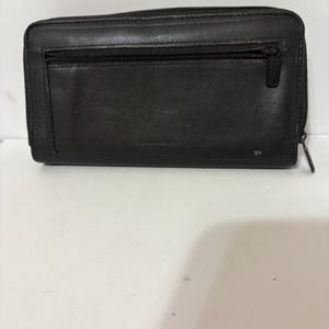 May include: Black leather wallet with a zipper closure and a smaller zippered pocket on the front. The wallet has a rectangular shape and appears to be made of genuine leather. The text "GENUINE LEATHER" is visible on the front.