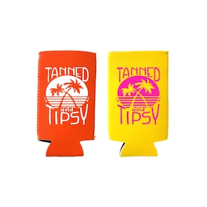 Może przedstawiać: Dwa neoprenowe ochraniacze na puszki, jeden pomarańczowy, a drugi żółty, z tekstem "Tanned and Tipsy" i grafiką palmy.
