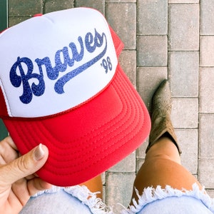 May include: A red and white baseball cap with a blue and white embroidered logo that says "Braves '98".