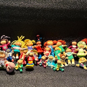 Peut inclure: Une grande collection de petites figurines miniatures Cabbage Patch Kids représentant divers personnages avec des cheveux en laine, des tenues colorées et des poses variées. Le groupe comprend des poupées en robes, tenues de sport et vêtements décontractés.