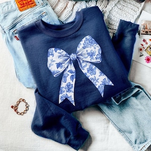 May include: A navy blue sweatshirt with a white and blue floral bow design.