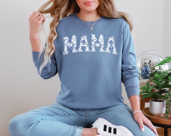 May include: A blue long-sleeved sweatshirt with the word "MAMA" printed in white with a floral pattern. The sweatshirt is worn by a person with long blonde hair.