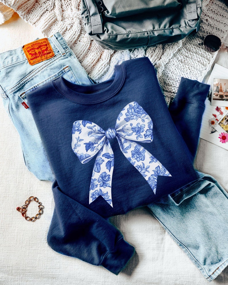 May include: A navy blue sweatshirt with a white and blue floral bow design.
