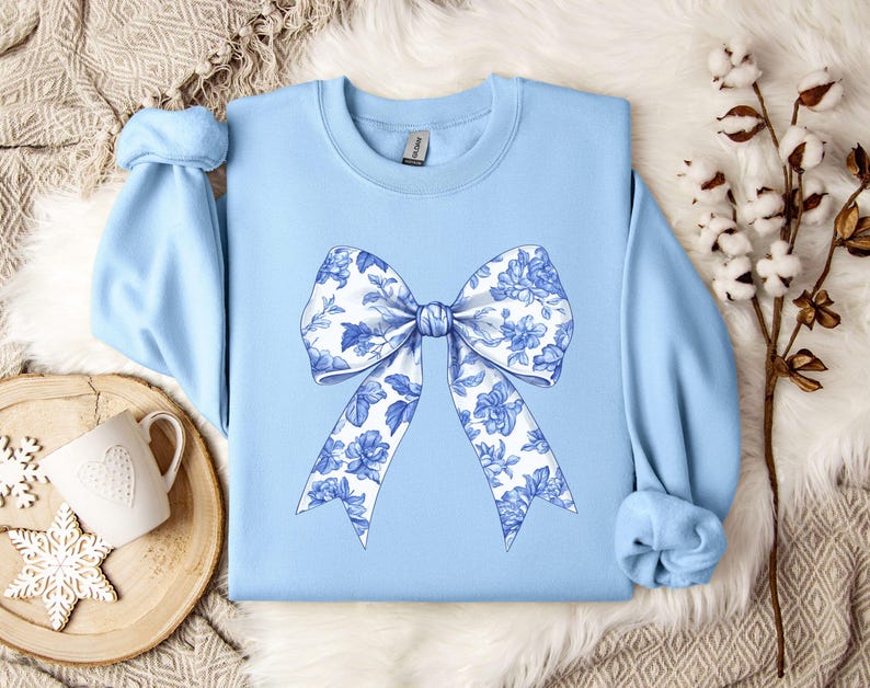 May include: A light blue sweatshirt with a large white and blue floral bow design on the front.
