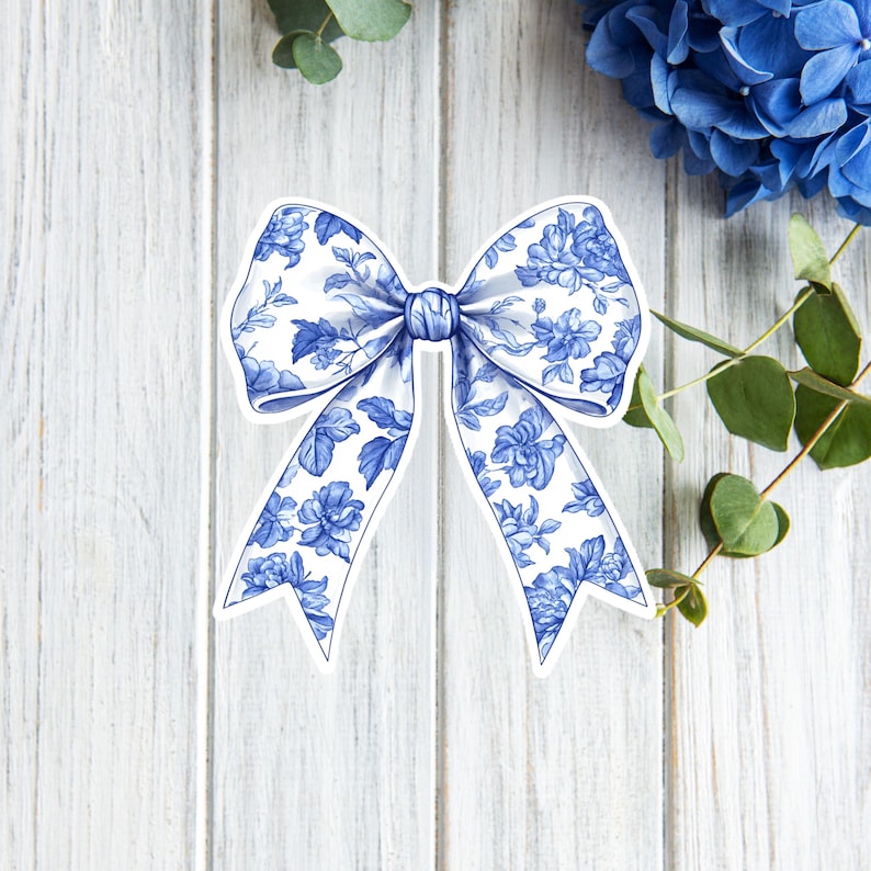 May include: A blue and white floral patterned bow with a white background. The bow is tied in a knot and the ends of the bow are curled.