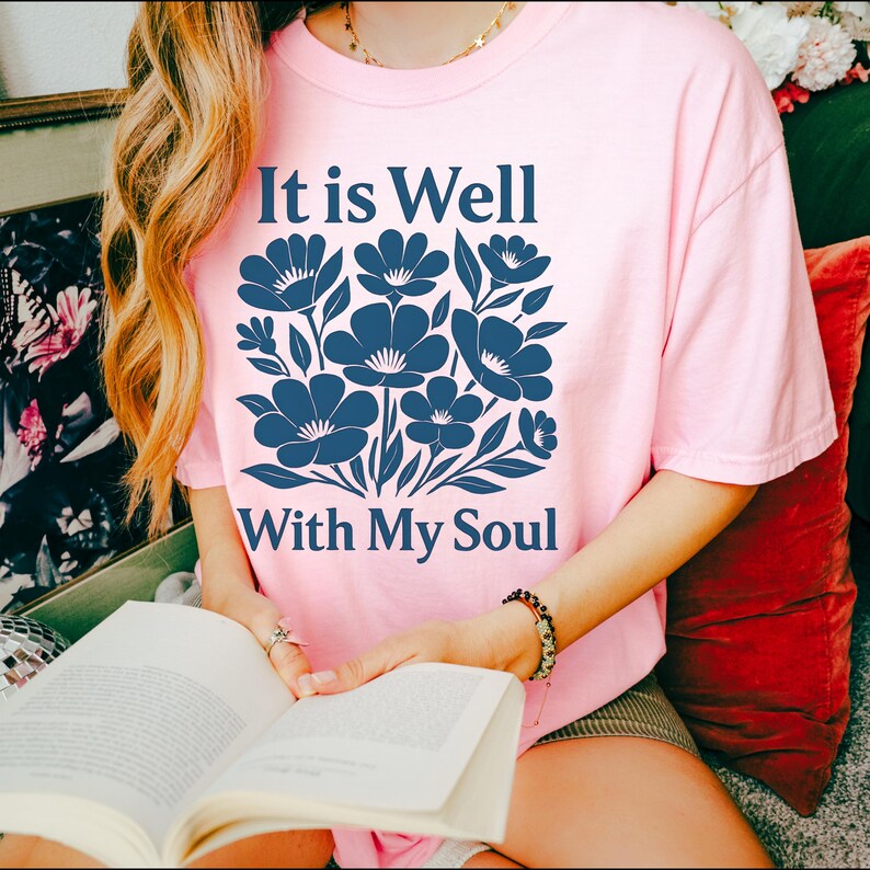 May include: A pink t-shirt with a blue floral design and the text "It is Well With My Soul".