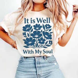 May include: A white t-shirt with a blue floral design and the text "It is Well With My Soul".