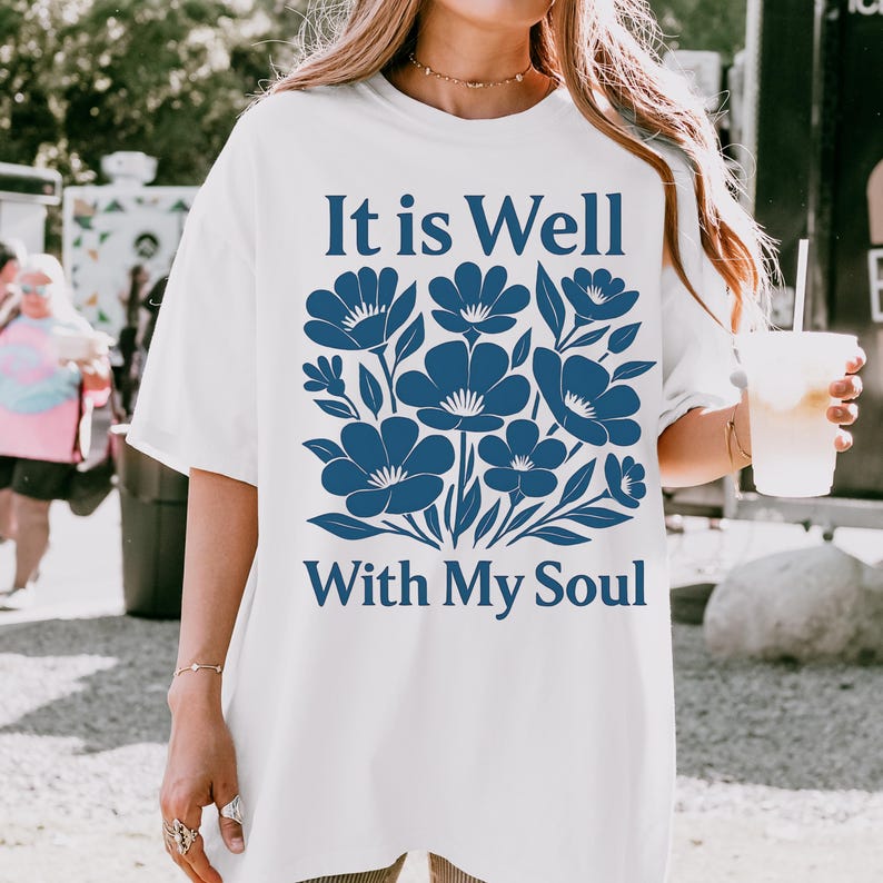 May include: White t-shirt with a blue floral design and the text "It is Well With My Soul".