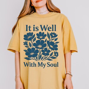 May include: A yellow t-shirt with a blue floral design and the text "It is Well With My Soul".