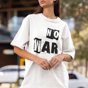 May include: A white t-shirt with the words "NO WAR" in a bold, black, distressed font. The shirt has short sleeves and a relaxed fit. The text is arranged in a blocky, graphic style, conveying a message of peace.