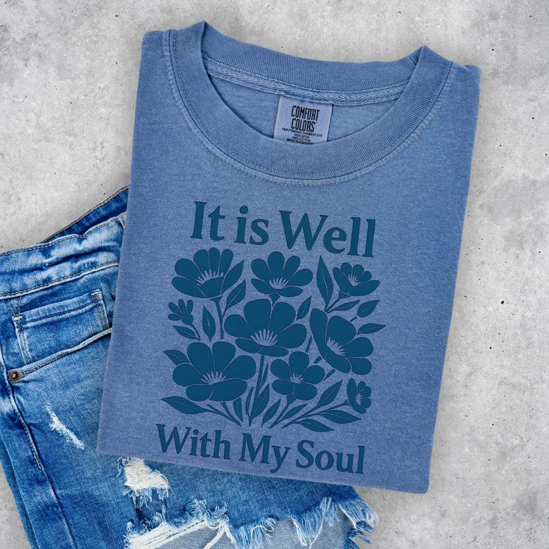 May include: A blue t-shirt with a floral design and the text "It is Well With My Soul".