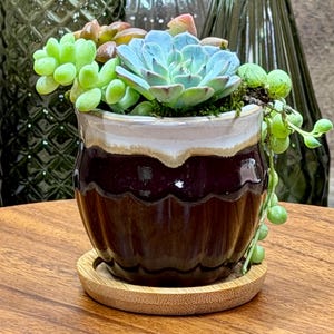 May include: A white ceramic mug with a black handle and the text "But First, Coffee" in a bold, black font. The mug is set against a blurred background, suggesting a cozy setting.
