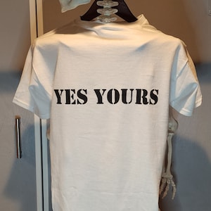Puede incluir: Camiseta blanca con el texto "YES YOURS" impreso en negro en la parte posterior.