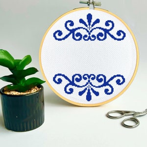 Puede incluir: Un aro de bordado blanco con un diseño floral azul. El diseño es un patrón repetitivo de espirales y hojas.