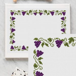 Peut inclure: Un motif de point de croix avec une bordure de vigne avec des raisins violets et des feuilles vertes. Le motif est sur un tissu blanc et est prêt à être brodé.