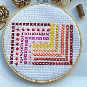 Könnte beinhalten: Ein farbenfrohes Kreuzstich-Design in einem hölzernen Stickrahmen. Das Design zeigt eine Vielzahl von Stichen in Rot-, Orange-, Gelb- und Rosatönen.
