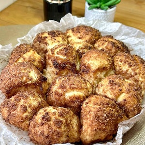 Könnte beinhalten: Nahaufnahme eines Tabletts mit frisch gebackenen, goldbraunen Zimtschnecken. Die Schnecken sind auf Backpapier angeordnet und großzügig mit Zimtzucker bestreut. Ein köstlicher Genuss.