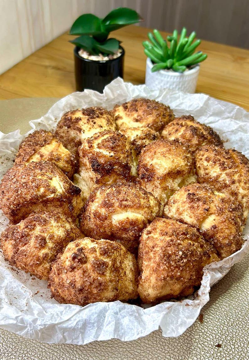 May include: A close-up shot of a tray of freshly baked, golden-brown cinnamon rolls. The rolls are arranged on a sheet of parchment paper, with a generous coating of cinnamon sugar. The baked goods are a delicious treat.