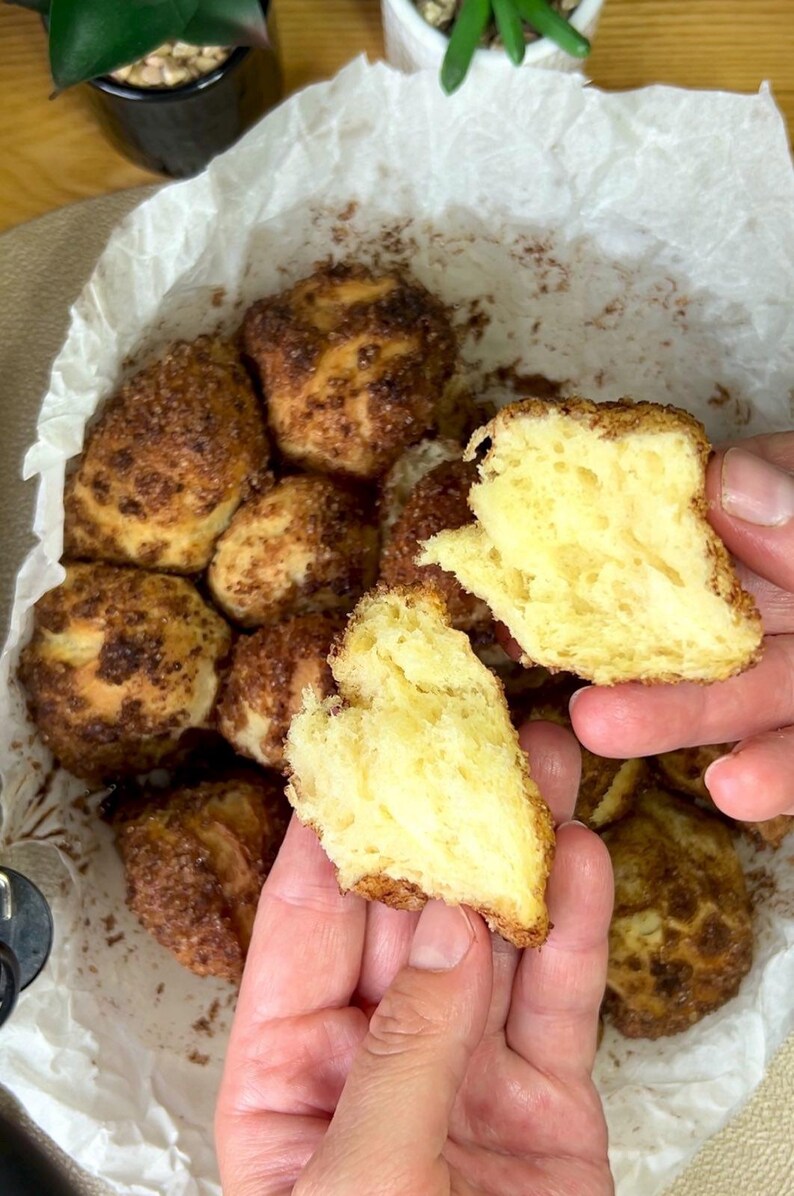 May include: Close-up of freshly baked, golden-brown monkey bread. The bread is torn open, revealing a soft, yellow interior. The exterior is coated in a sweet, cinnamon-sugar crust, perfect for a delicious treat.