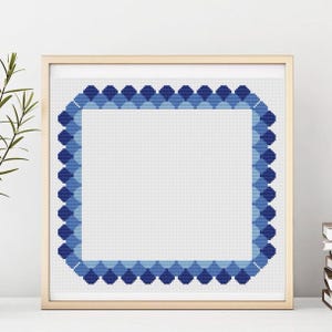 May include: Framed cross-stitch art featuring a square design with a border of blue diamond shapes. The border transitions from light to dark blue, surrounding a white center. The frame is a light wood color.