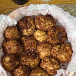 May include: A close-up shot of a pink plate filled with golden-brown, round pastries. The pastries are coated in a dark brown sugar and cinnamon mixture, sitting on white parchment paper. The image suggests a dessert or snack.