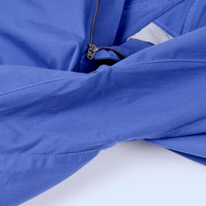 Puede incluir: Primer plano de una chaqueta azul con cremallera y panel de malla. La chaqueta est&aacute; hecha de una tela lisa y tiene detalles de costura visibles. La cremallera es de color plateado.