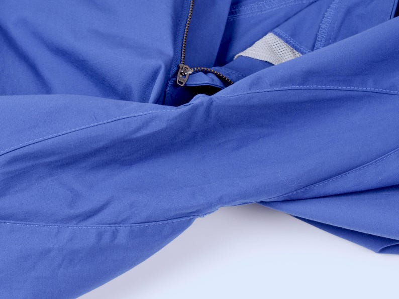 Puede incluir: Primer plano de una chaqueta azul con cremallera y panel de malla. La chaqueta est&aacute; hecha de una tela lisa y tiene detalles de costura visibles. La cremallera es de color plateado.
