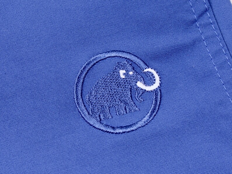 Puede incluir: Primer plano de una tela azul con un logotipo bordado. El logotipo es un c&iacute;rculo con un dise&ntilde;o de mamut lanudo en azul y blanco. La tela tiene una textura sutil y una costura visible.