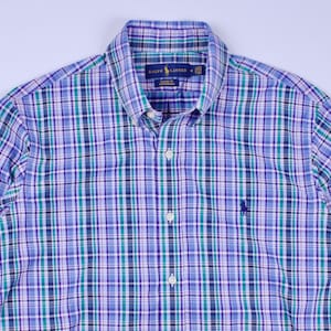 May include: A button-down shirt with a plaid pattern in shades of blue, green, and white. The shirt features a button-down collar, a chest pocket, and the embroidered logo of a polo player. The shirt is made of a lightweight fabric.