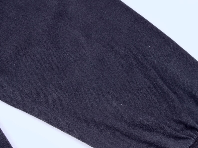 May include: Close-up of a dark navy blue long-sleeved garment. The fabric appears to be a soft knit material, with a slight sheen. The sleeve is gathered at the wrist with a ribbed cuff.