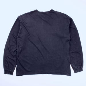 May include: A dark gray long-sleeve shirt. The shirt has a crew neck and long sleeves with ribbed cuffs. The fabric appears to be a soft, worn material. The shirt is laid flat on a white surface.