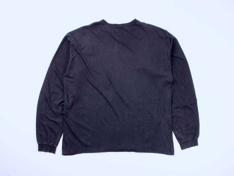 May include: A dark gray long-sleeve shirt. The shirt has a crew neck and long sleeves with ribbed cuffs. The fabric appears to be a soft, worn material. The shirt is laid flat on a white surface.