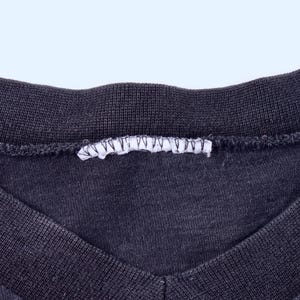 May include: Close-up of a dark gray V-neck shirt. The neckline and collar are ribbed, and a white tag is sewn into the back of the collar. The fabric has a slightly worn appearance.
