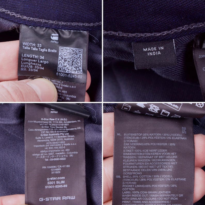 May include: Close-up of several tags attached to a pair of dark blue denim jeans. The tags display information about the jeans' width, length, and composition, including cotton, lyocell, and polyester. One tag reads "Made in India."