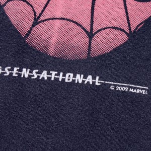 May include: Close-up of a dark blue t-shirt with a pink and black spiderweb design. The word "SENSATIONAL" is printed in white, along with the copyright "&copy; 2002 MARVEL".