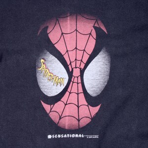May include: A navy blue graphic featuring the mask of Spider-Man. The mask is red with a black web pattern and white eye shapes. The word "Spider-Man" is in yellow script. The word "SENSATIONAL" is printed below the mask.