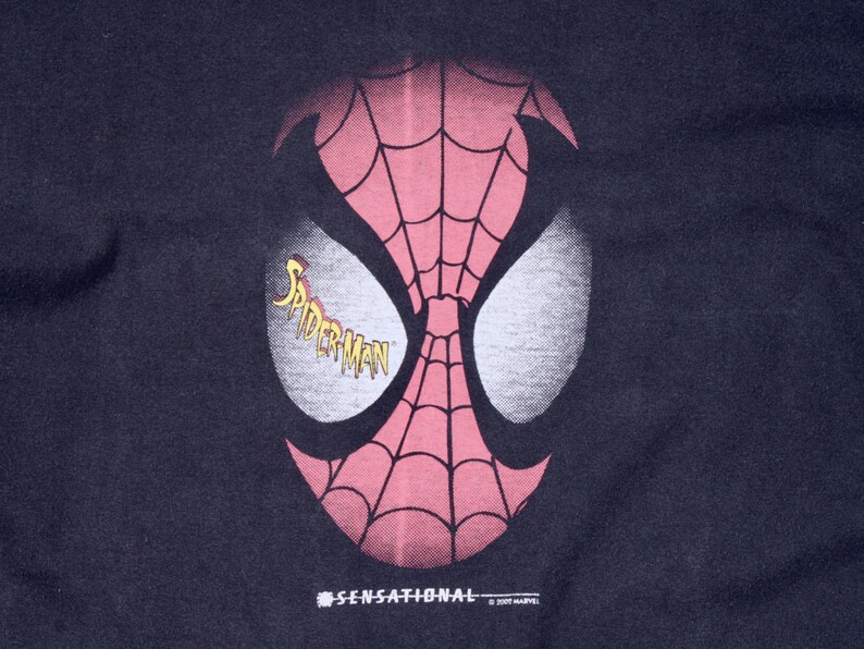 May include: A navy blue graphic featuring the mask of Spider-Man. The mask is red with a black web pattern and white eye shapes. The word "Spider-Man" is in yellow script. The word "SENSATIONAL" is printed below the mask.