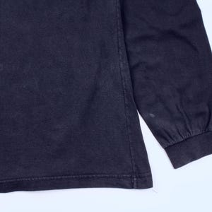 May include: A dark navy blue long-sleeve shirt. The sleeve cuff is visible, along with the hem of the shirt. The fabric appears to be a soft cotton blend. The shirt is a solid color with no visible graphics or patterns.
