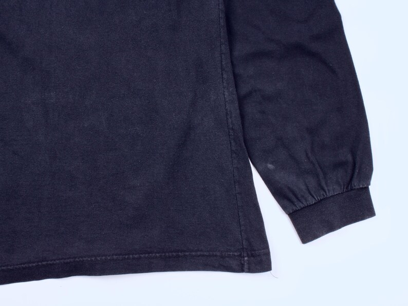 May include: A dark navy blue long-sleeve shirt. The sleeve cuff is visible, along with the hem of the shirt. The fabric appears to be a soft cotton blend. The shirt is a solid color with no visible graphics or patterns.