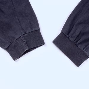 May include: Close-up of two dark gray long-sleeve shirt cuffs. The cuffs are ribbed and the sleeves are slightly wrinkled. The background is plain white.