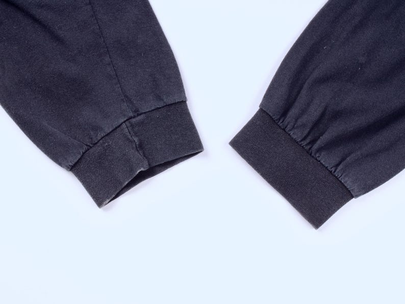 May include: Close-up of two dark gray long-sleeve shirt cuffs. The cuffs are ribbed and the sleeves are slightly wrinkled. The background is plain white.
