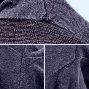 May include: Close-up of dark gray fabric with visible stitching and small imperfections. The image shows the texture and construction of the material, highlighting the details of the garment's seams and potential wear.