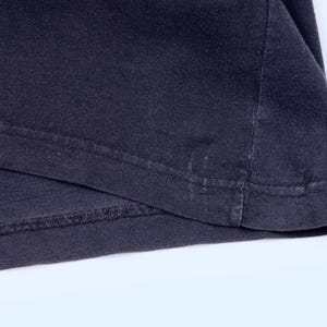 May include: Close-up of a dark gray t-shirt hem. The fabric is folded over, revealing the stitched seam and the edge of the shirt. The material appears to be soft and slightly worn.