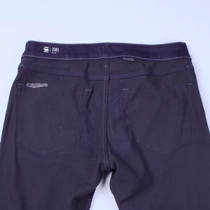 May include: Dark navy blue denim jeans with a dark blue waistband. The back of the jeans features two pockets and a small logo patch. The jeans have a straight leg cut and are made of a durable denim material.