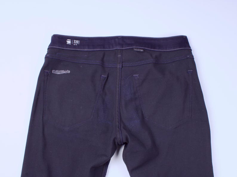 May include: Dark navy blue denim jeans with a dark blue waistband. The back of the jeans features two pockets and a small logo patch. The jeans have a straight leg cut and are made of a durable denim material.