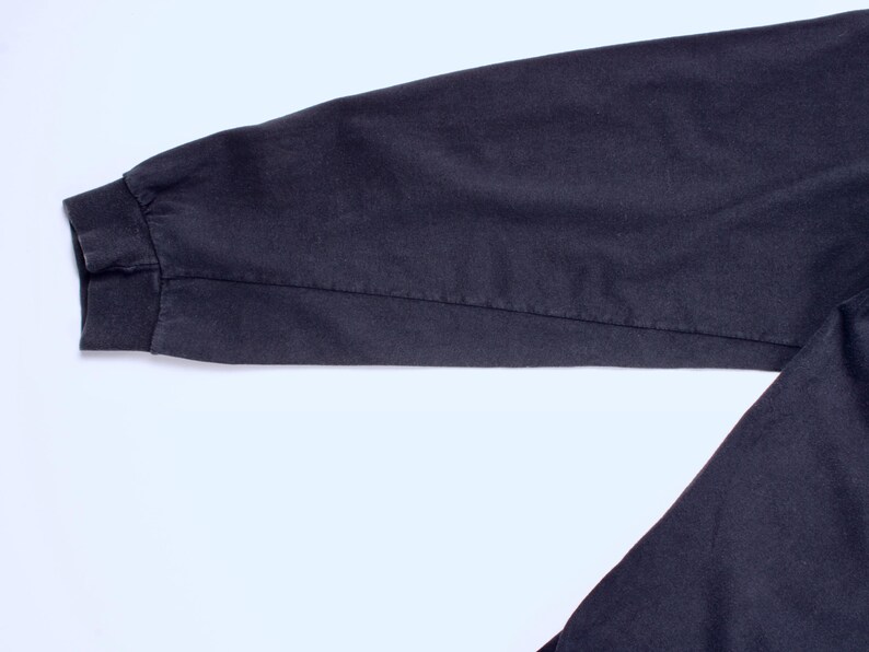 May include: Close-up of a dark navy blue long sleeve shirt sleeve. The sleeve has a ribbed cuff and a seam running down the length of the arm. The fabric appears to be a soft, durable material.