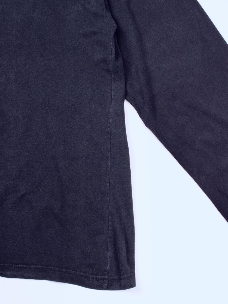 May include: A close-up of a black long-sleeve shirt. The shirt is made of a soft material and has a simple design. The sleeve is visible on the right side of the image.