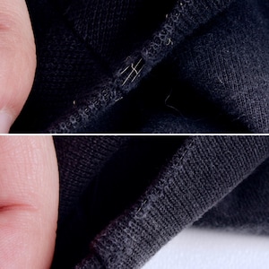 May include: Close-up of black fabric with visible stitching and a small tear. The fabric appears to be a knit material, with loose threads and a slightly worn texture. The image highlights the details of the textile.