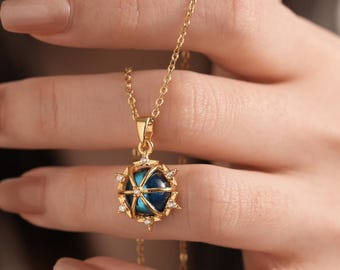 May include: A gold necklace with a blue and gold pendant. The pendant is a sphere with a star-shaped design and small clear stones.