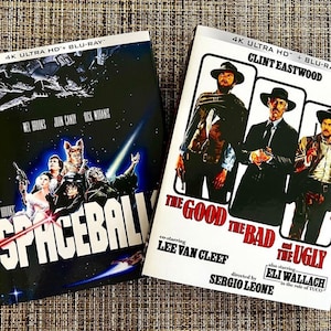 May include: Two 4K Ultra HD Blu-ray movie cases. The left case is for the movie "Spaceballs" and features a black background with a group of characters from the movie. The right case is for the movie "The Good, the Bad and the Ugly" and features a white background with a poster of the three main characters.